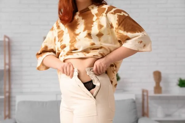 Image of woman trying to do her trousers up after pregnancy weight gain Lyme Regis