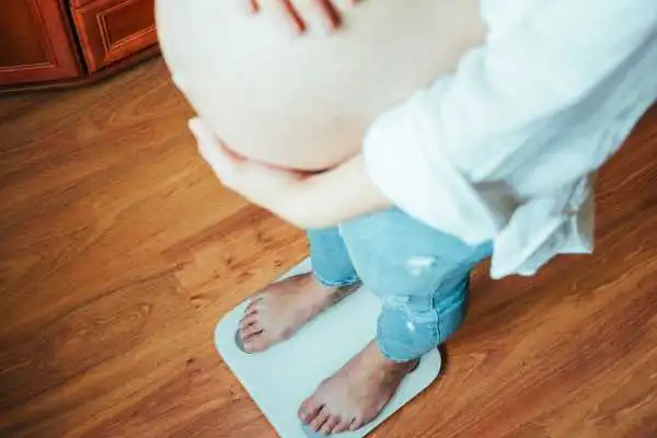 Image of woman weighing herself and experiencing weight gain through pregnancy Lyme Regis